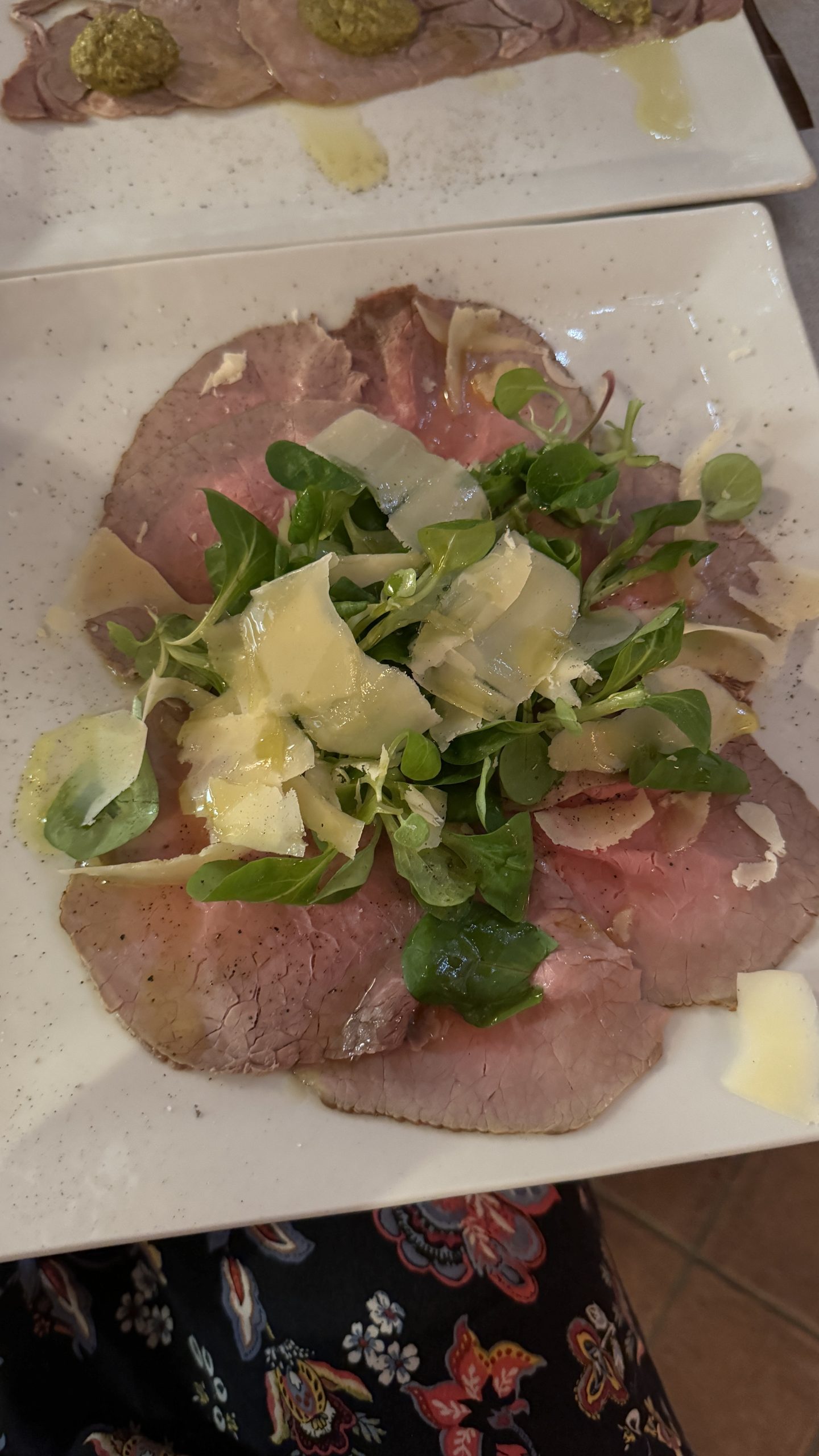 Thinly sliced Piedmontese beef arranged with greens, shaved cheese, and a refined garnish at a Langhe restaurant.