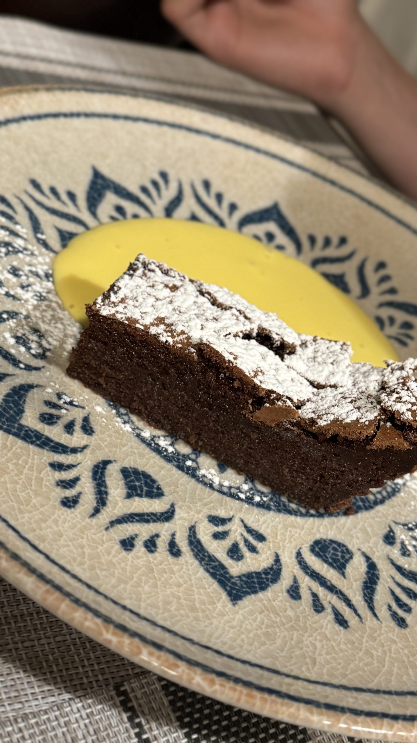 Elegant slice of chocolate cake dusted with sugar and served with a bright yellow sauce in Piedmont.