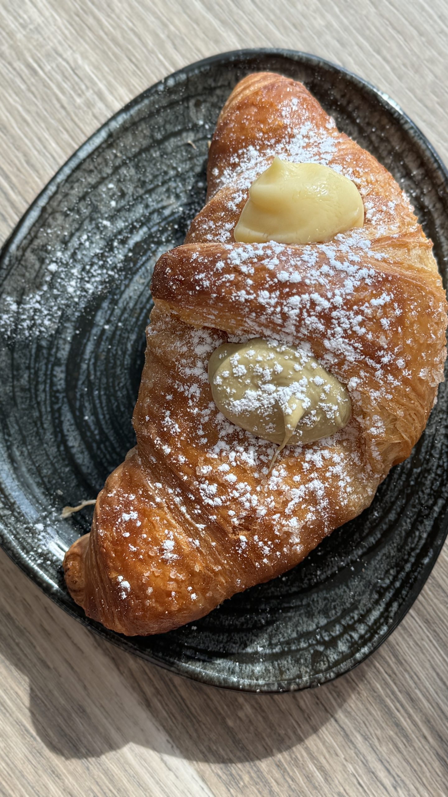 Powdered croissant filled with two pastry creams on a dark ceramic plate in Piedmont.