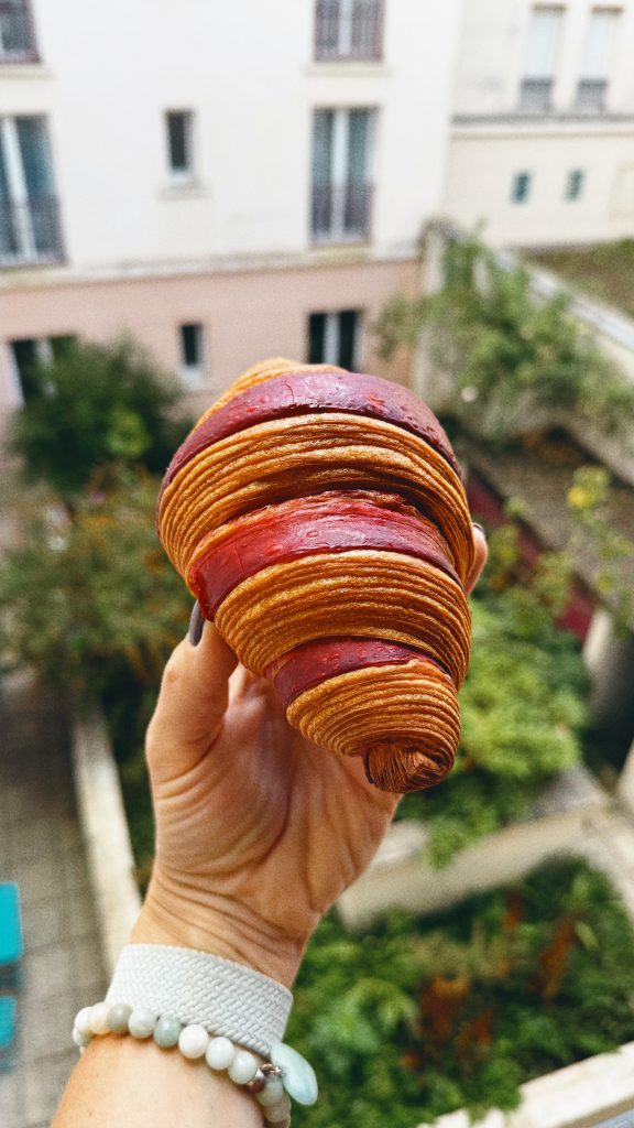 Raspberry-filled laminated croissant held against a courtyard in Maisons-Laffitte, France.