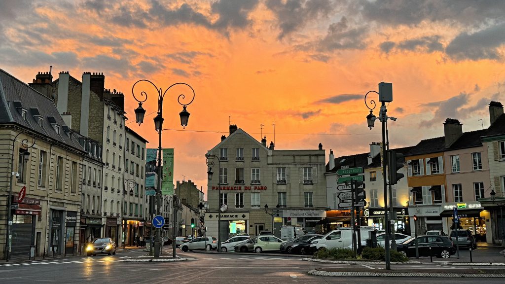 Maisons-Laffitte town center beneath a vivid orange evening sky near Paris, France.