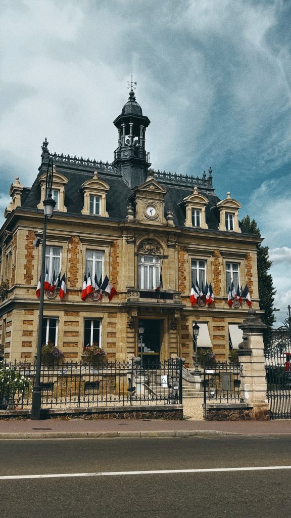 Historic town hall in Maisons-Laffitte decorated with French flags beneath a dramatic blue sky.