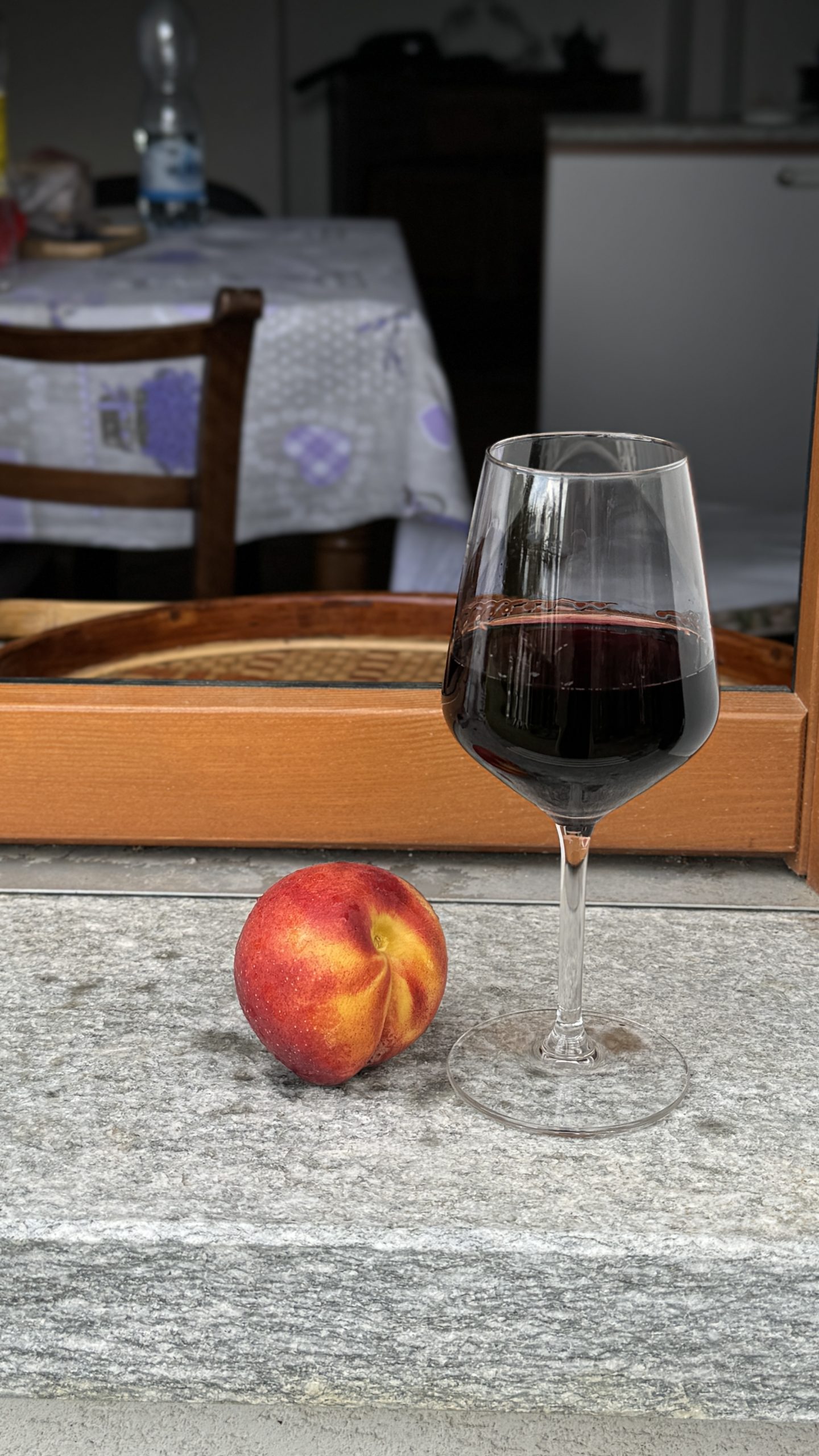 Glass of red wine and a ripe peach on a stone ledge at a family table in Piedmont.