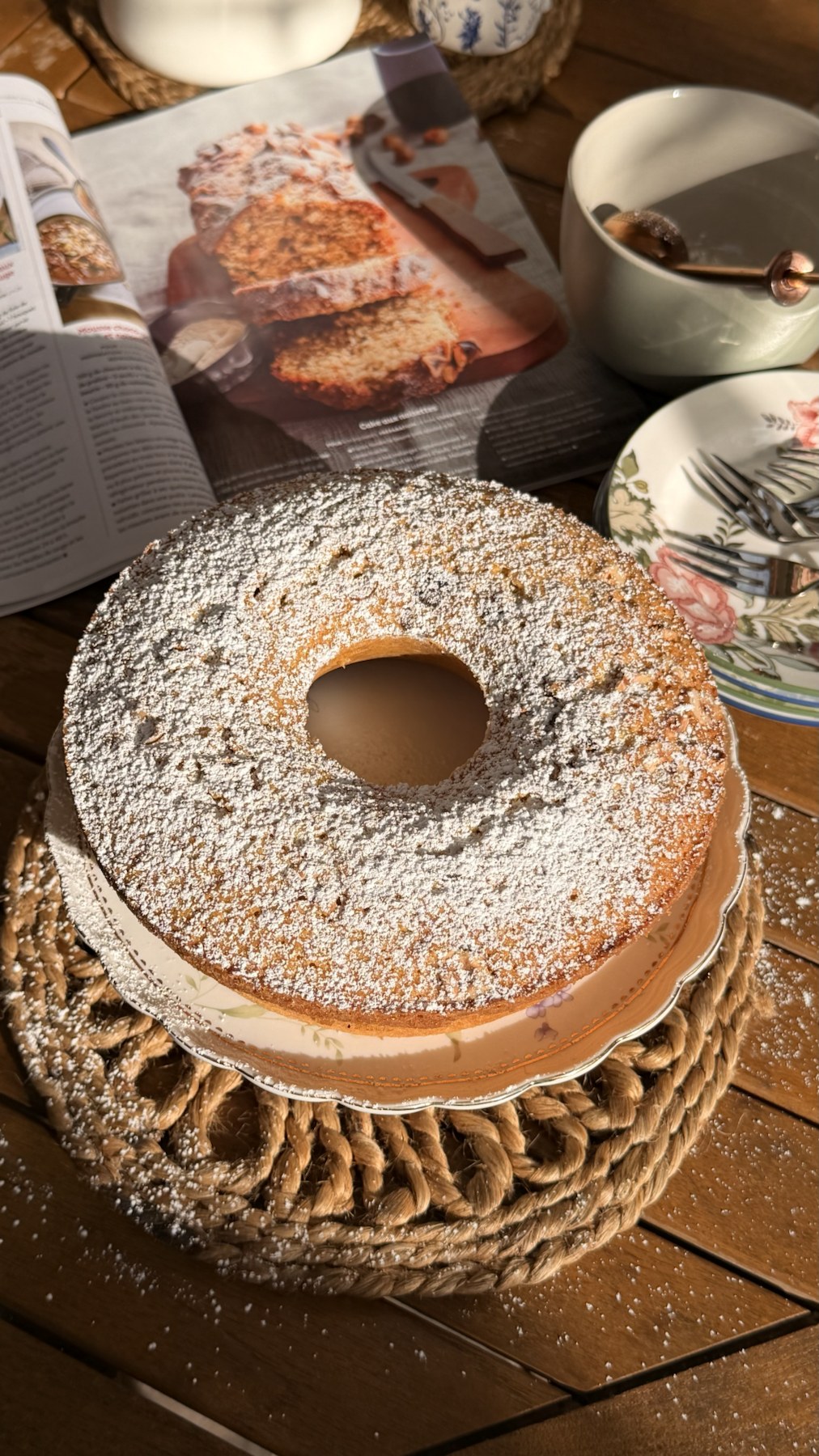 Finished Piedmont inspired hazelnut cake dusted with powdered sugar beside the open French magazine recipe.