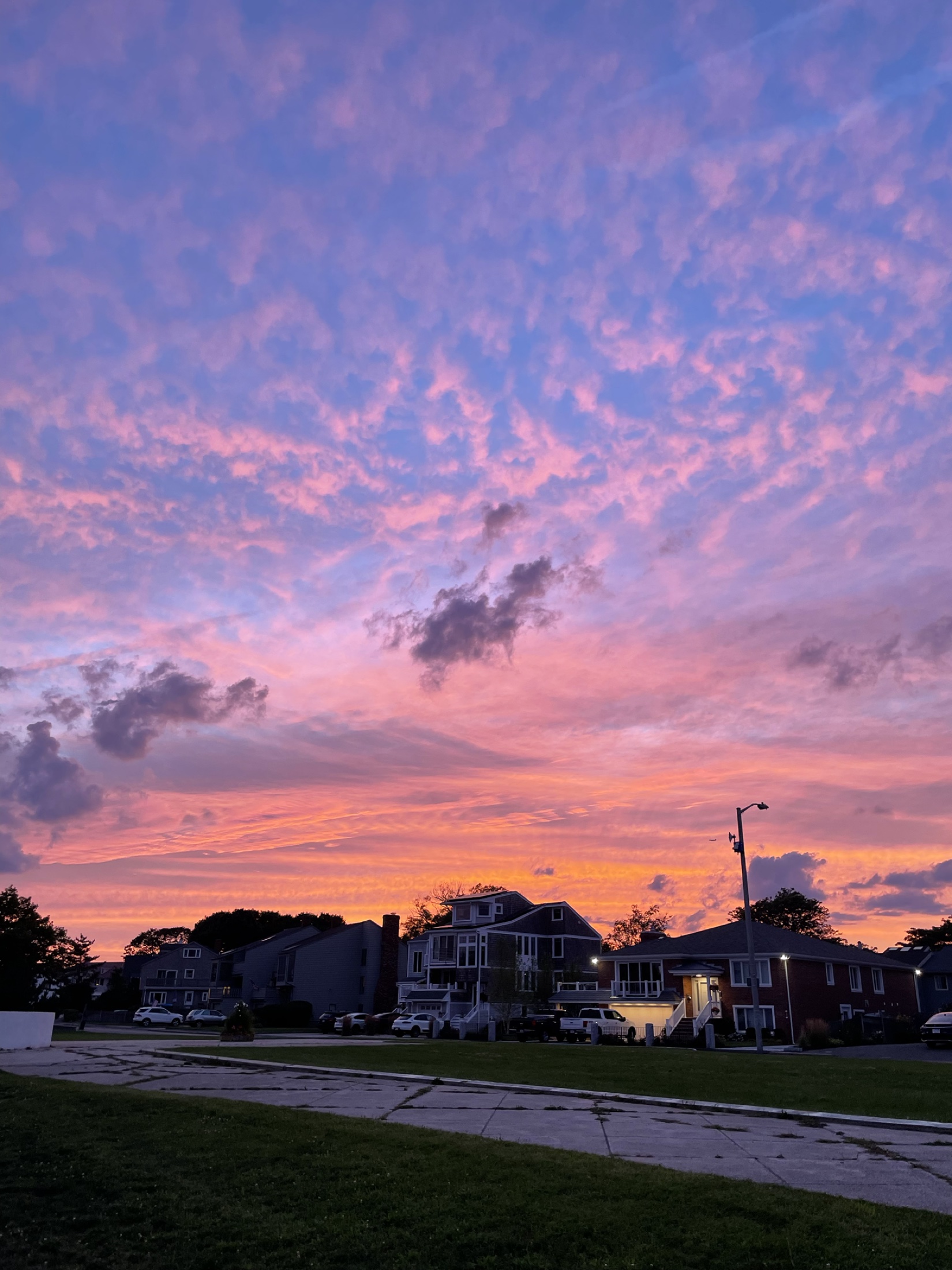 Pink, violet and coral clouds glowing over a neighborhood at an August sunset.