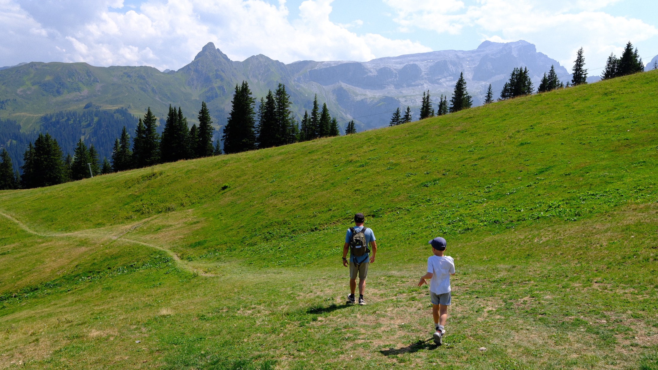 An adult and child walking across a high green meadow at Golm