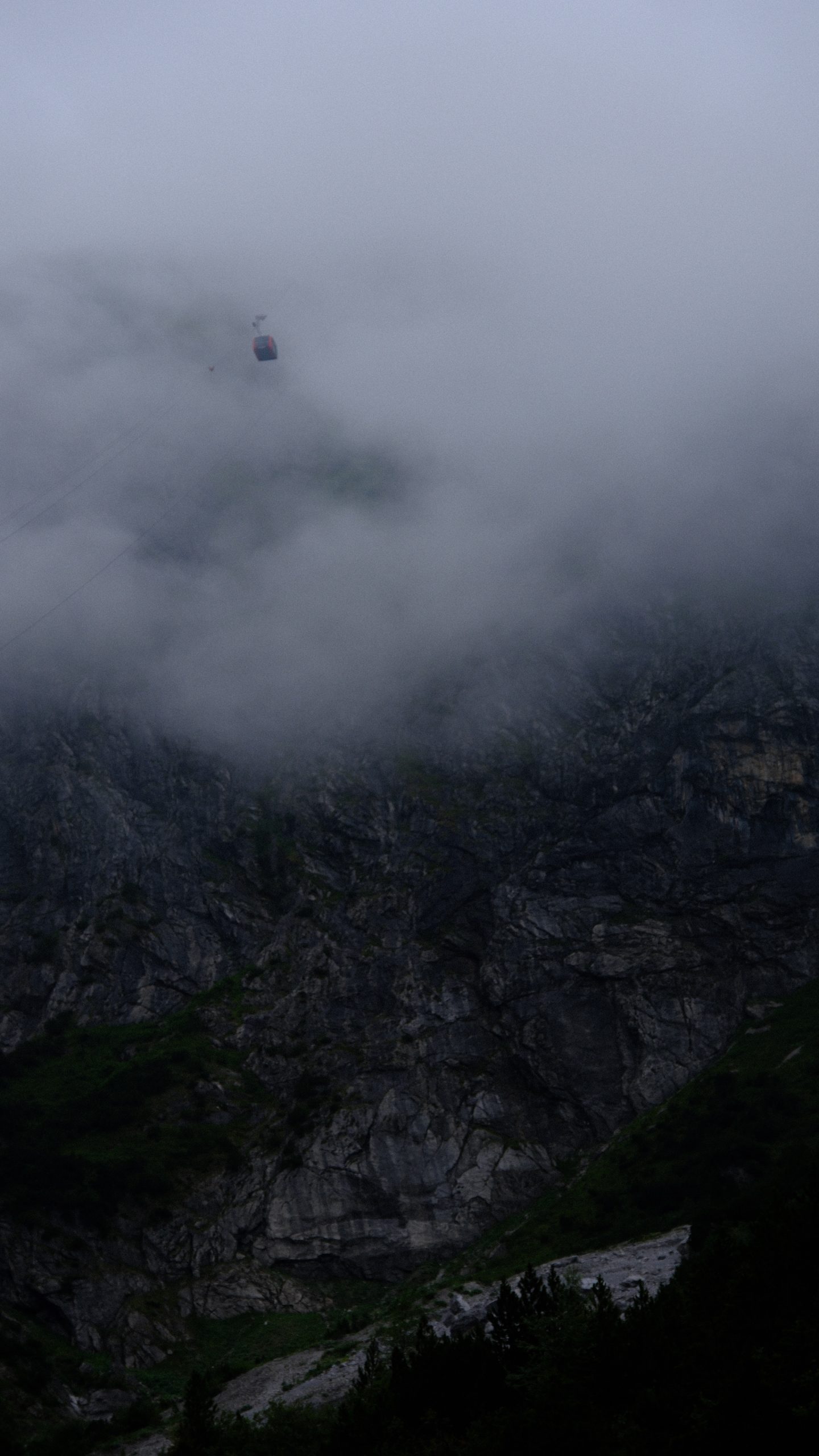 A red Lünerseebahn gondola climbing past a dark cliff into low cloud.