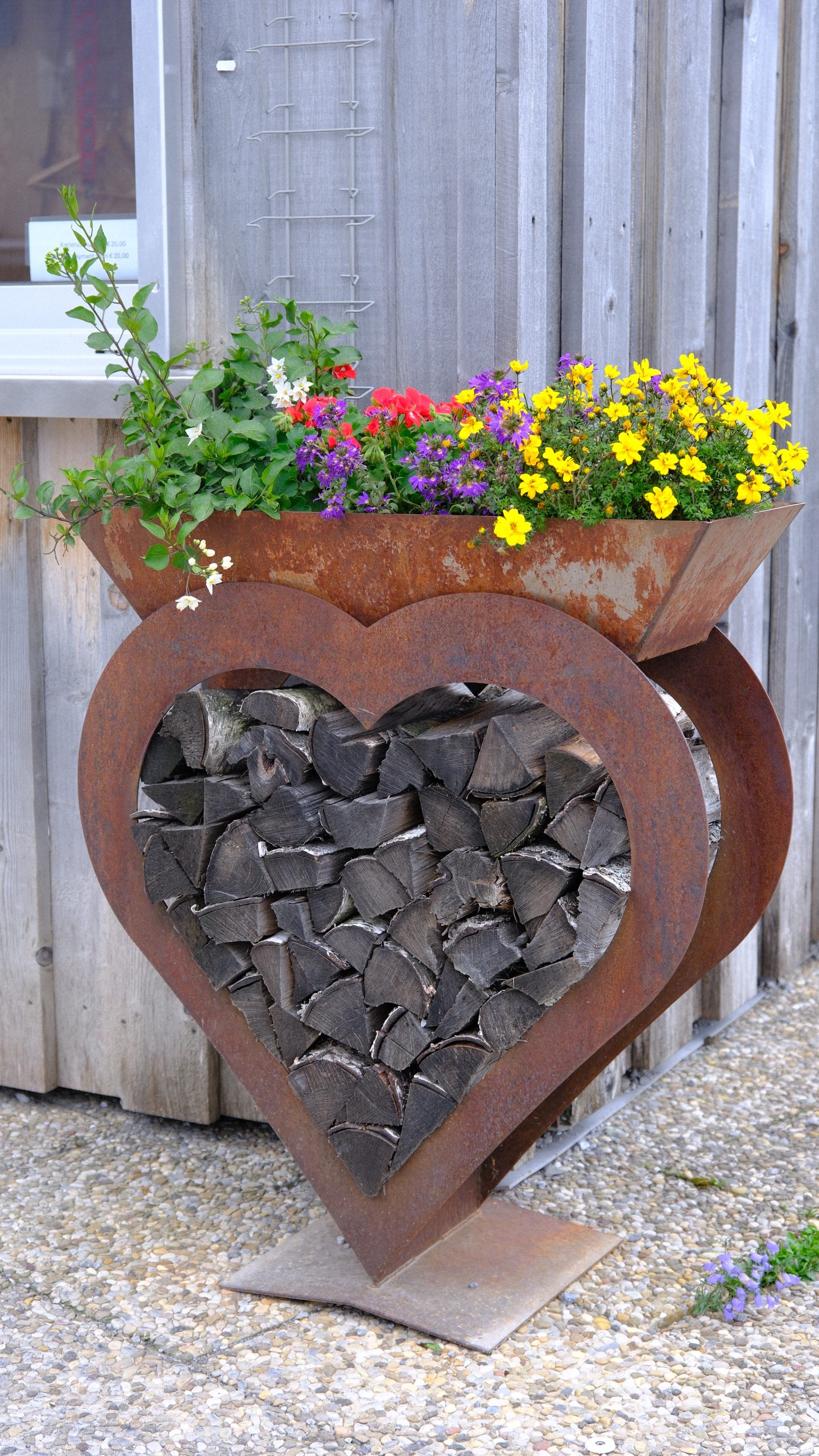 A rust-coloured metal heart filled with mountain stones and topped with flowers.