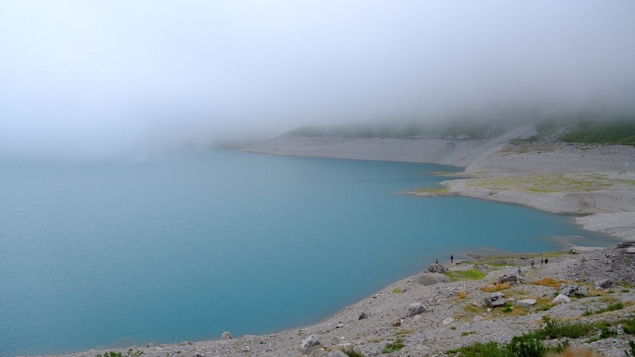 A wide curve of Lünersee with mountains hidden beneath a ceiling of fog.