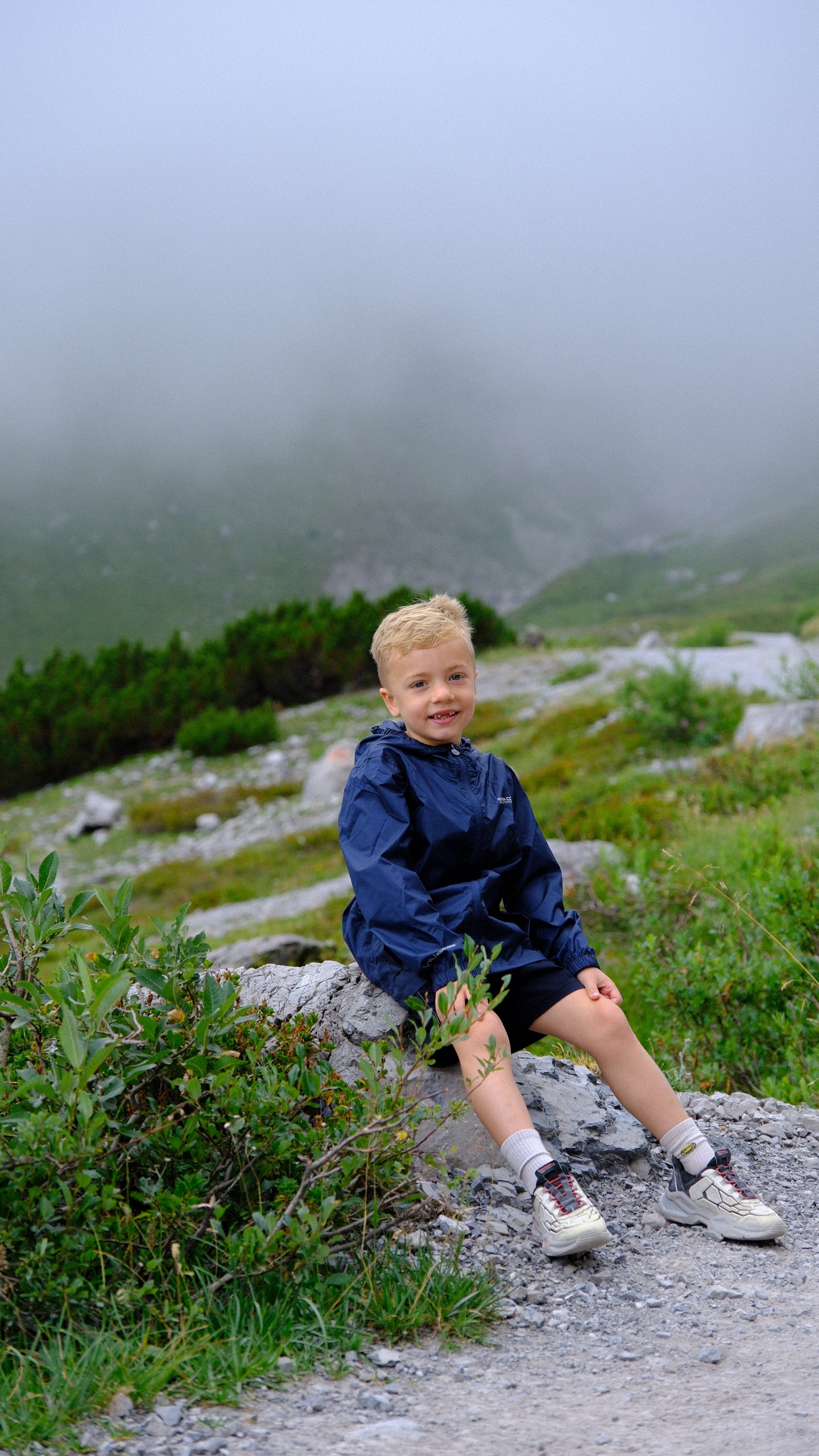 Chris sitting on a rock beside the wet mountain path, with mist drifting over the slope behind him.