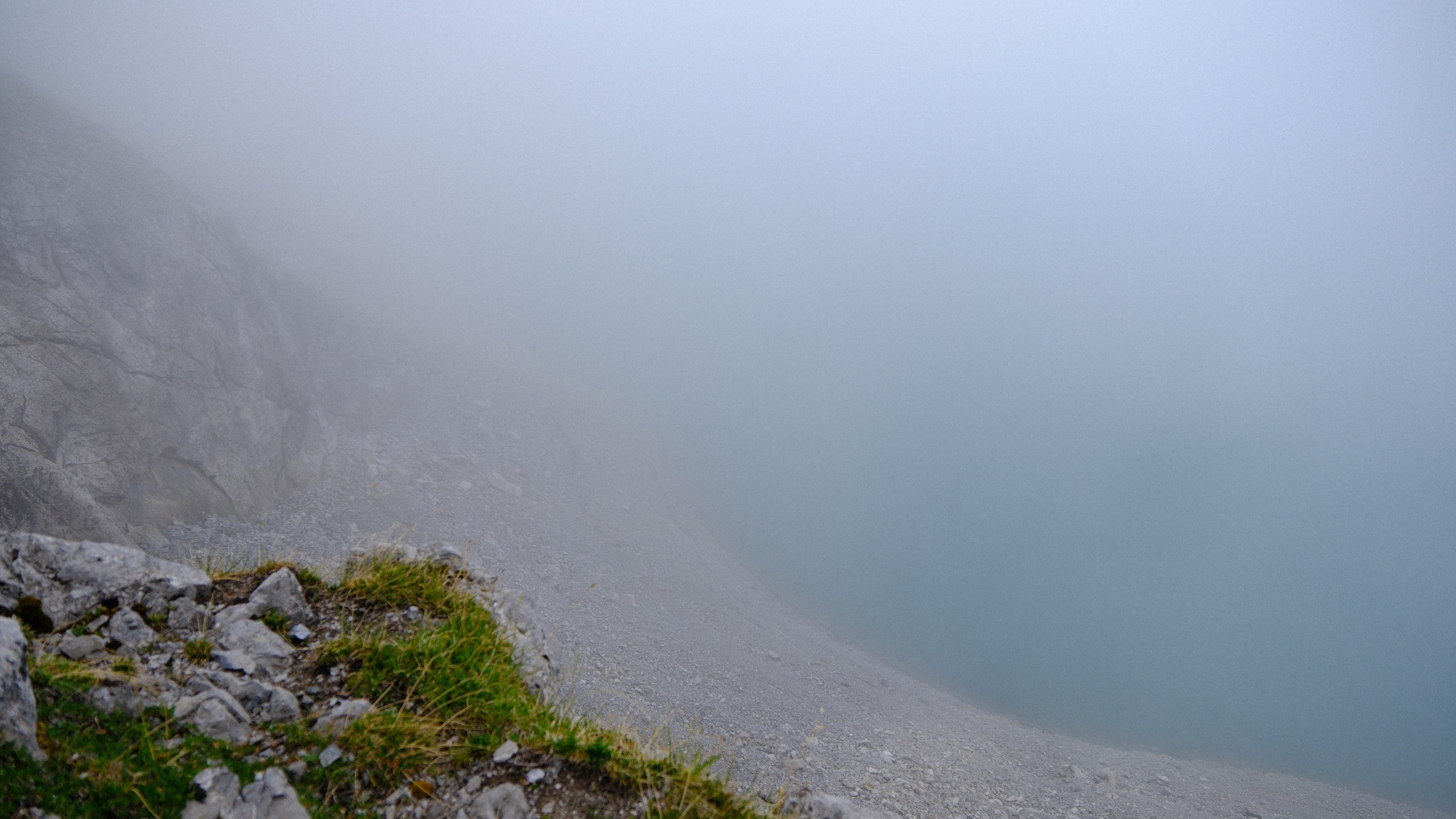 The blue edge of Lünersee dissolving into white cloud beneath a rocky slope.