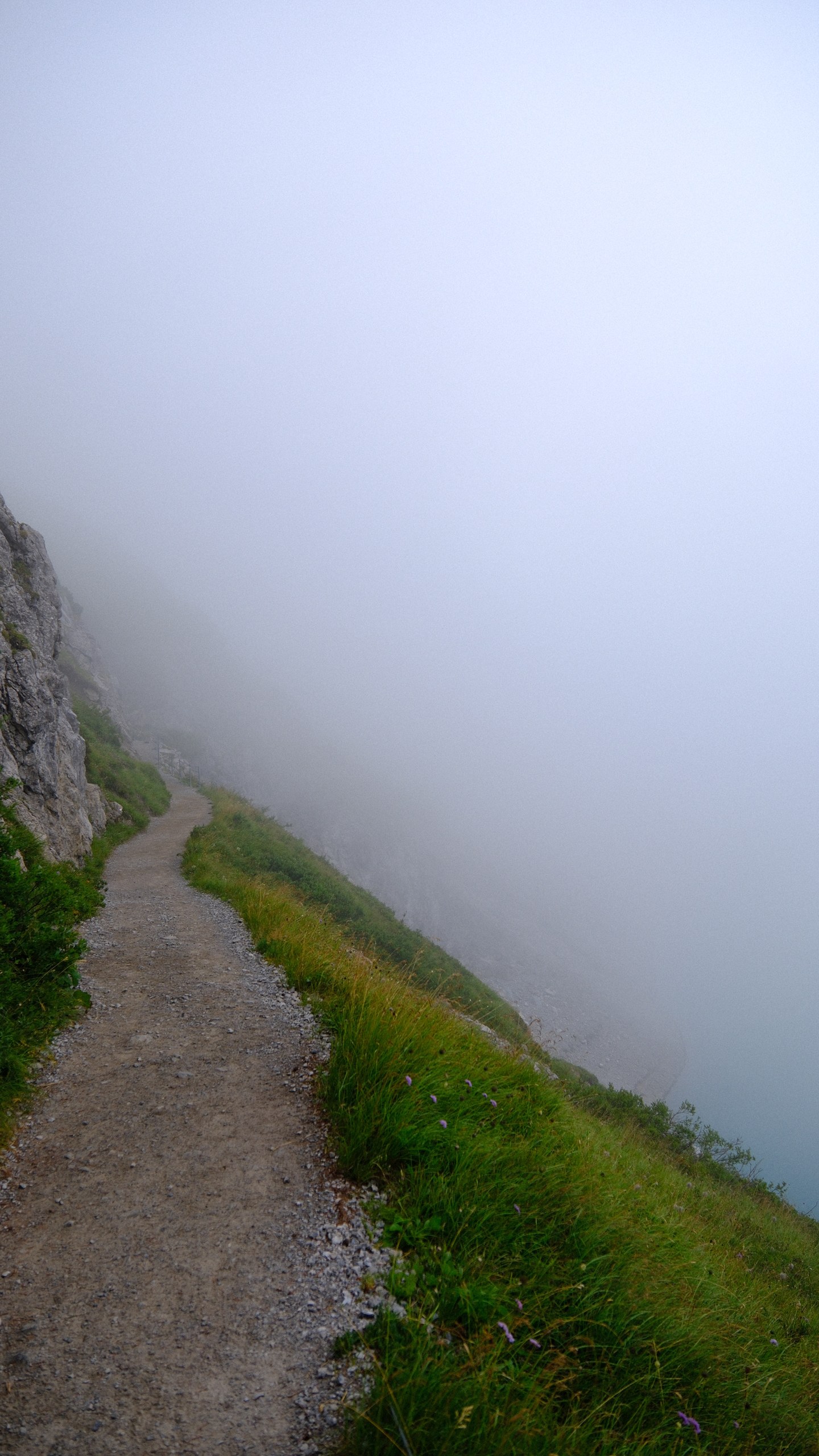 A narrow mountain path vanishing into thick white fog.