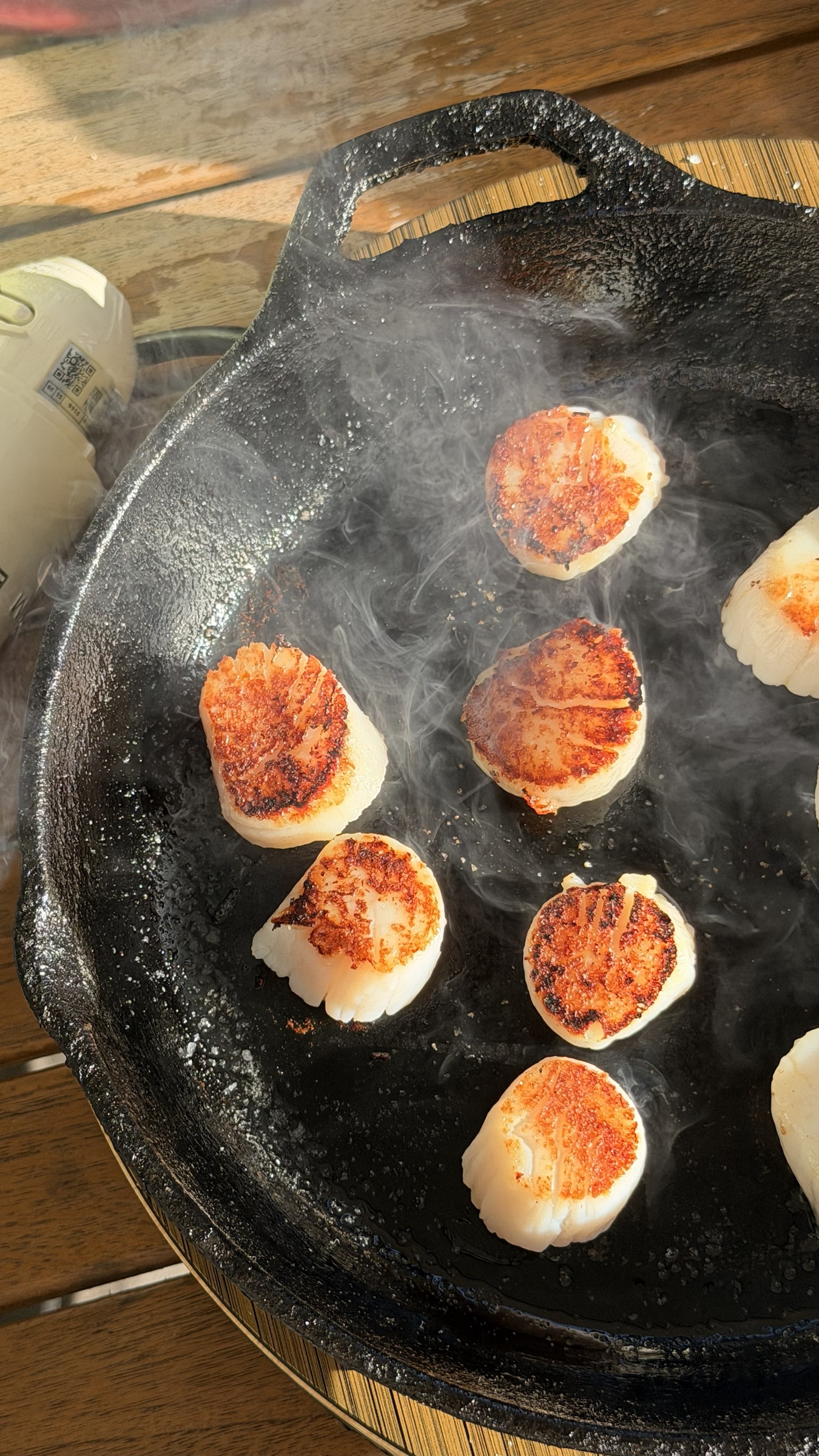 Golden seared scallops cooking in a black cast iron pan in afternoon sunlight.