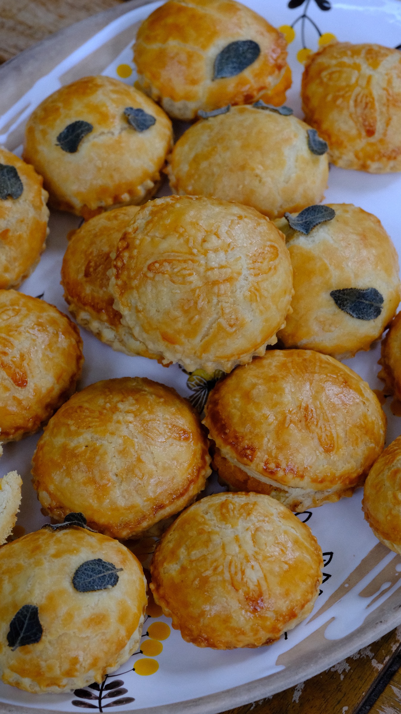 Finished golden hand pies with embossed tops and fresh sage arranged on a serving platter.