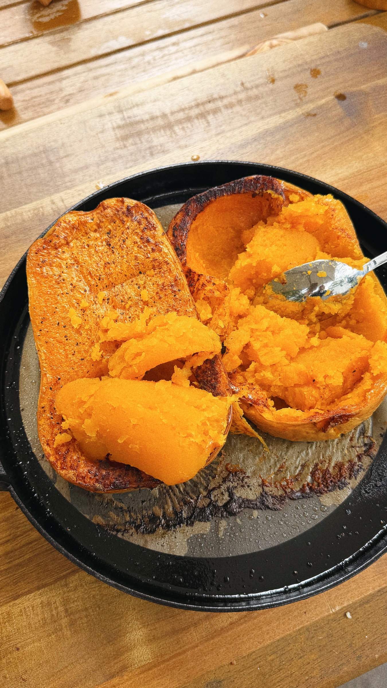 Roasted butternut squash being scooped from its deeply browned skin.