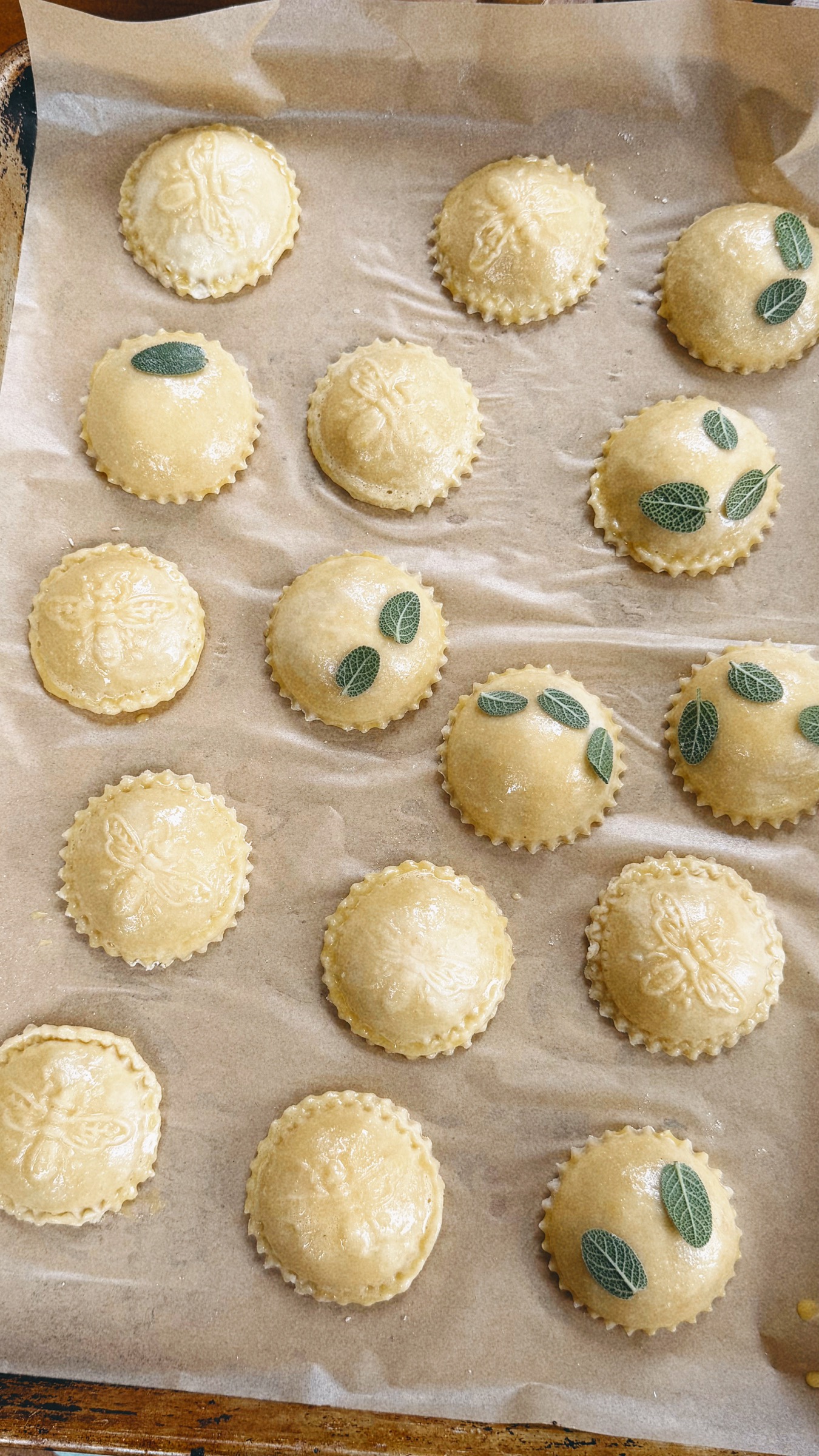 Unbaked round hand pies with embossed bee designs and fresh sage leaves on parchment.