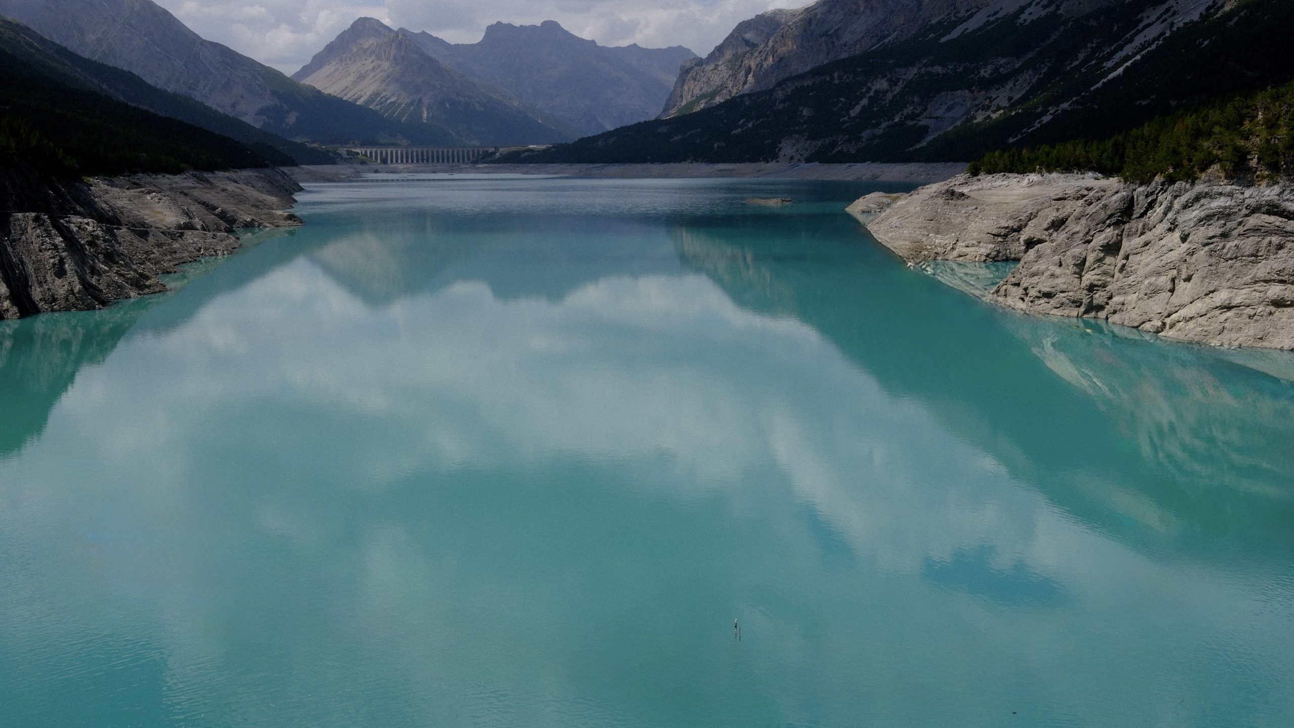 Turquoise water of Lago di Cancano reflecting clouds beneath dark mountains