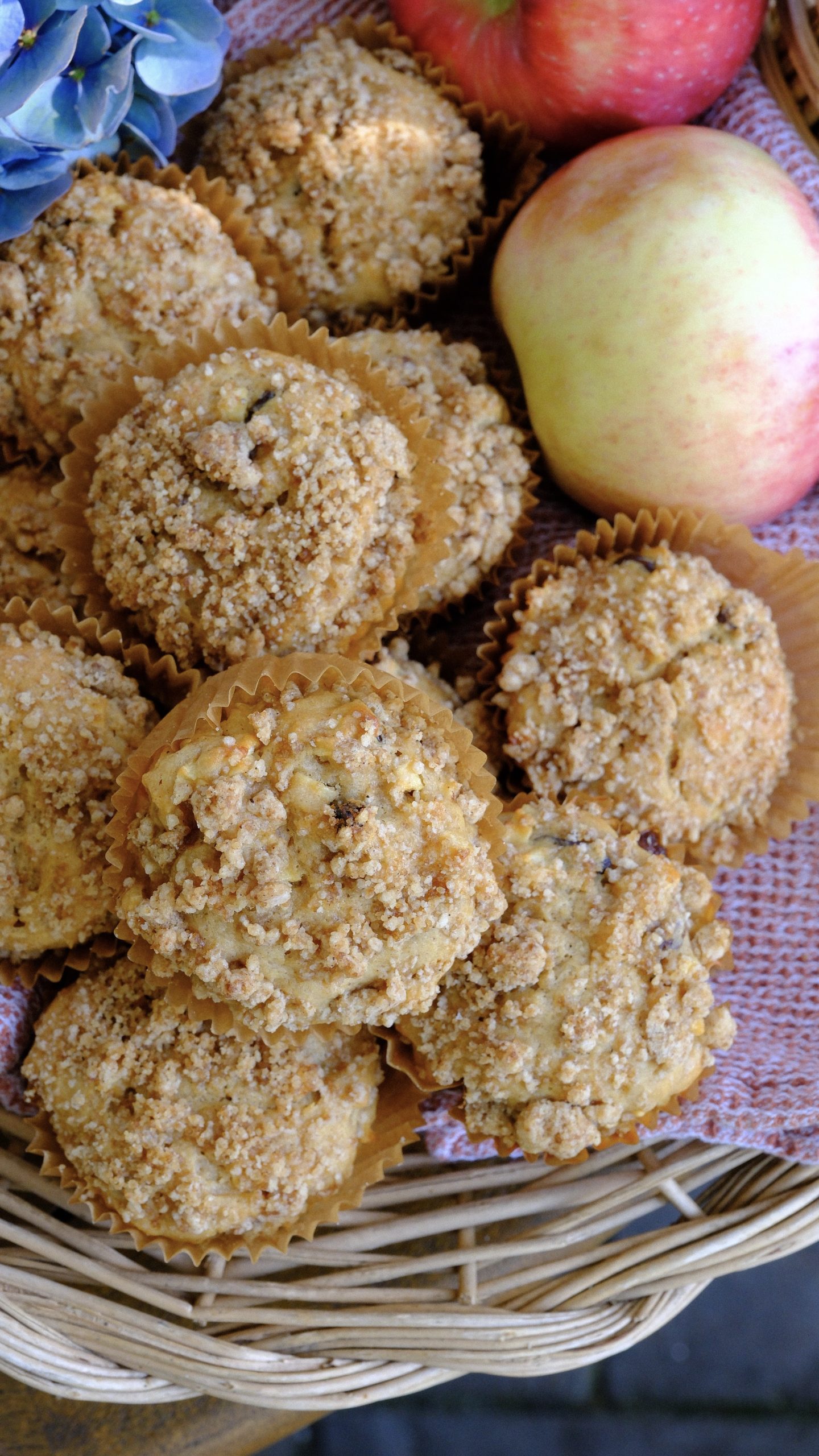 Apple cinnamon raisin muffins with brown sugar streusel arranged in a wicker basket beside fresh apples