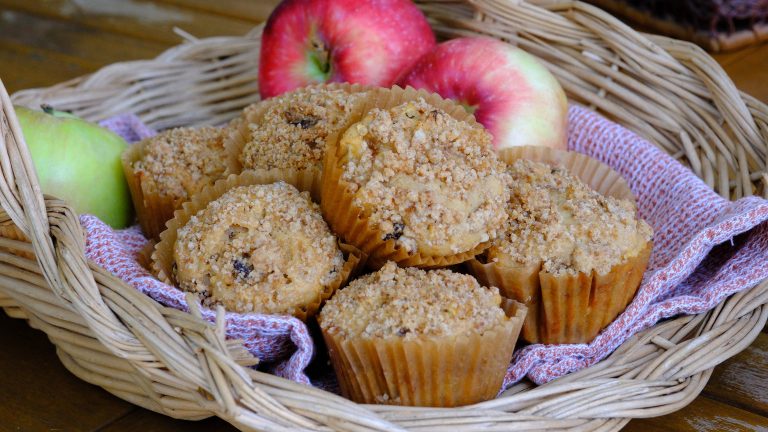 Apple cinnamon raisin muffins with brown sugar streusel in a wicker basket with fresh apples