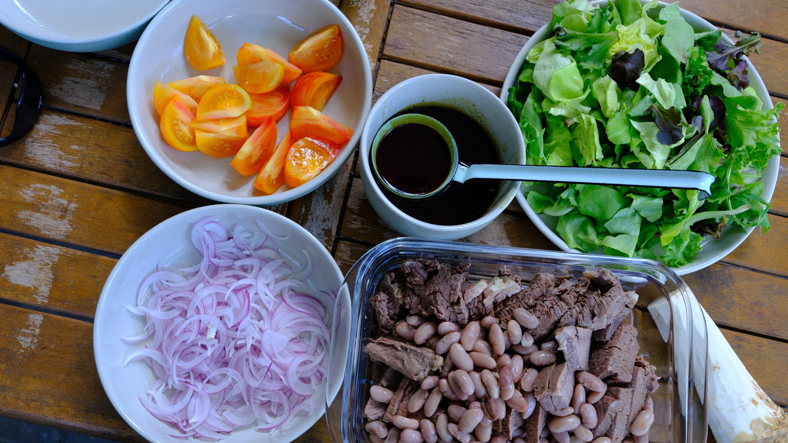 Sliced red onion, orange tomatoes, mixed greens, beef, runner beans, and dark pumpkin seed oil arranged for the salad