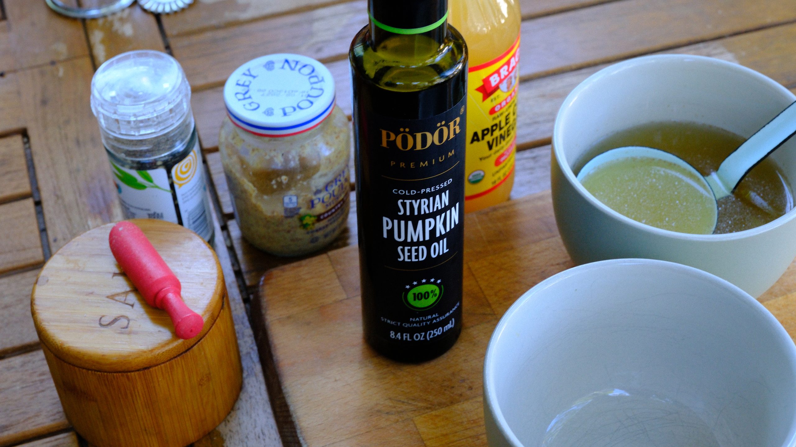 Bottle of Styrian pumpkin seed oil beside apple vinegar, mustard, salt, and warm beef broth