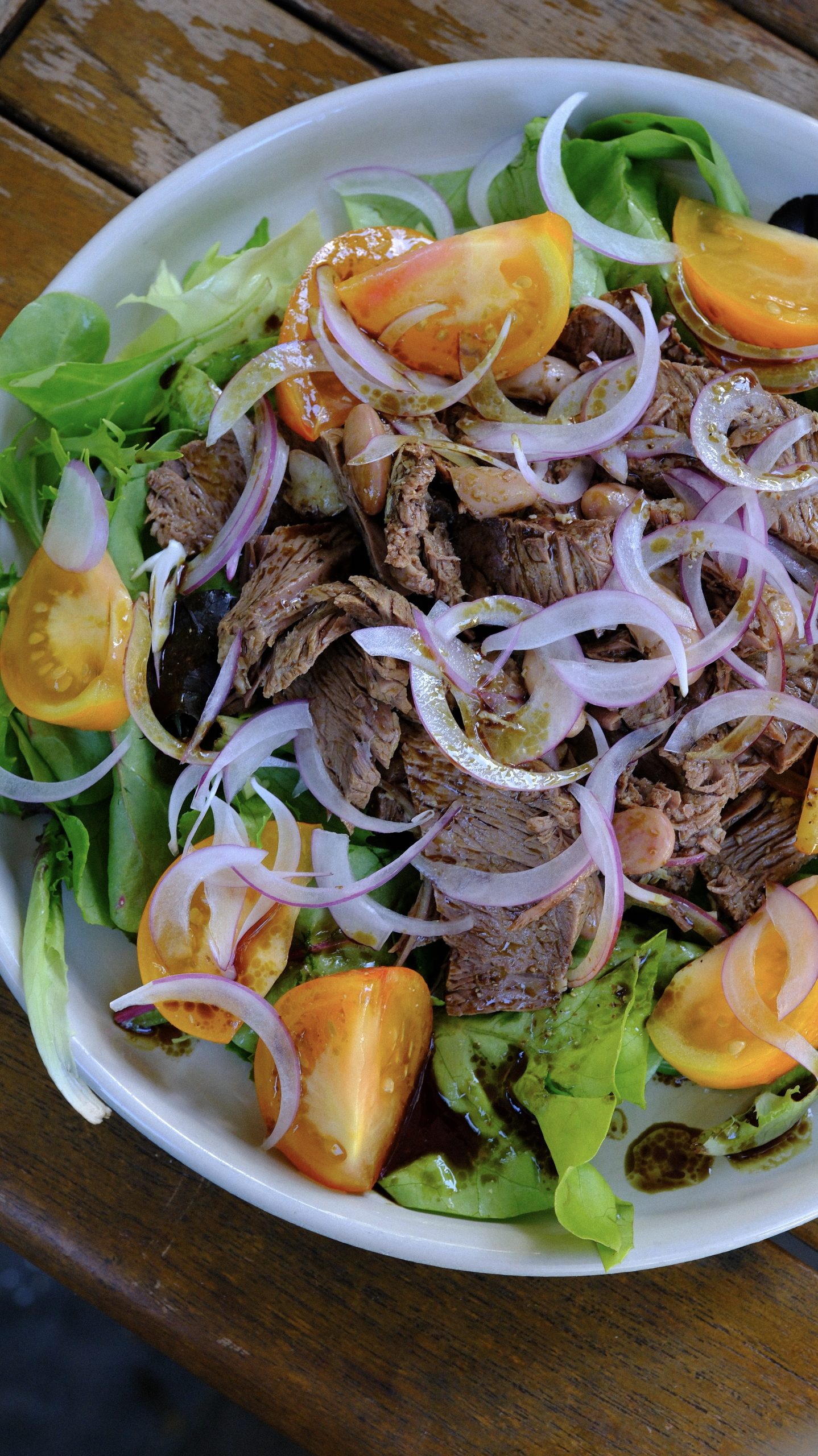 Styrian boiled beef salad with runner beans, red onion, orange tomatoes, and mixed greens in a white bowl