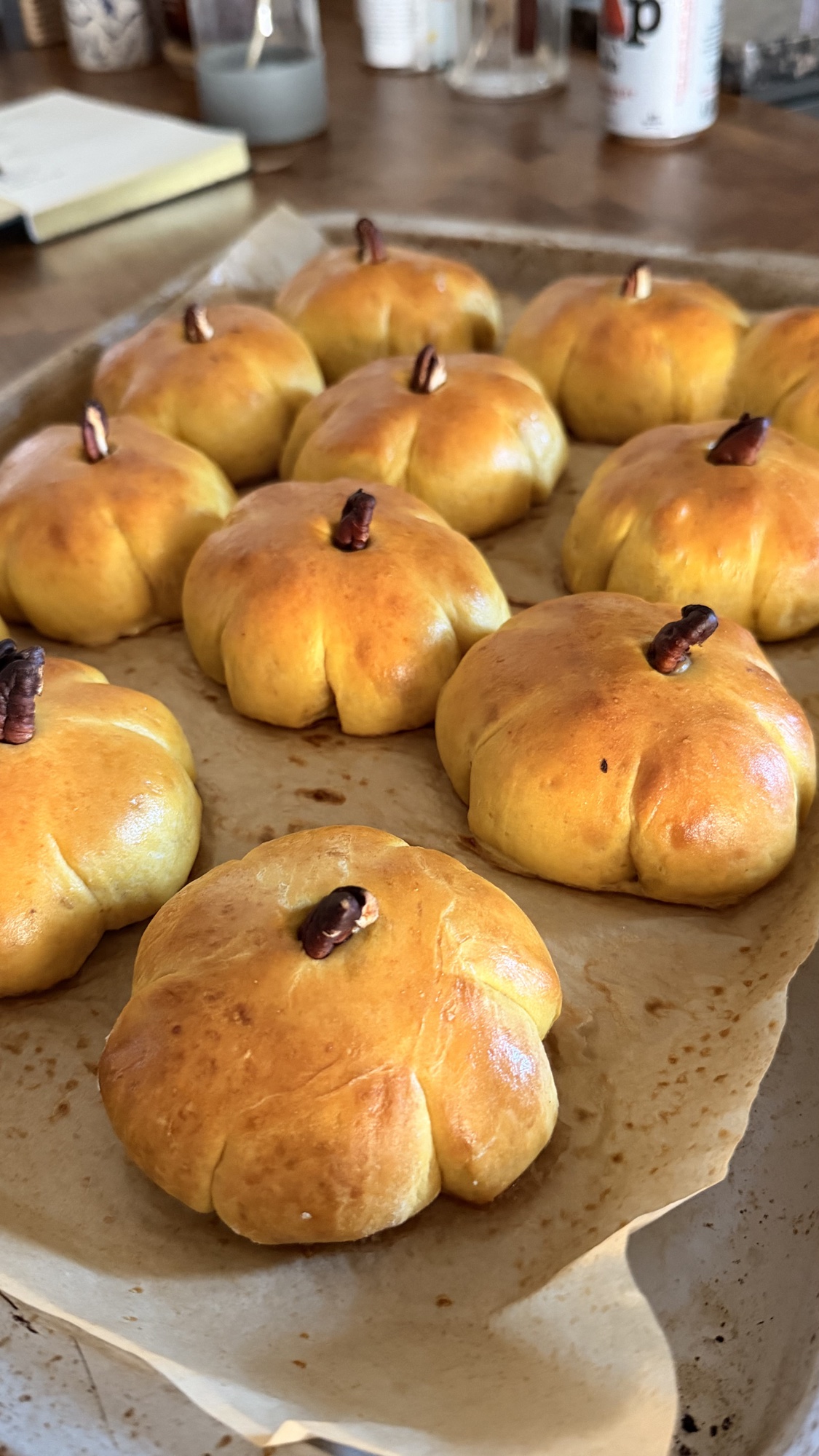 Golden pumpkin-shaped dinner rolls with pecan stems arranged on a parchment-lined baking sheet
