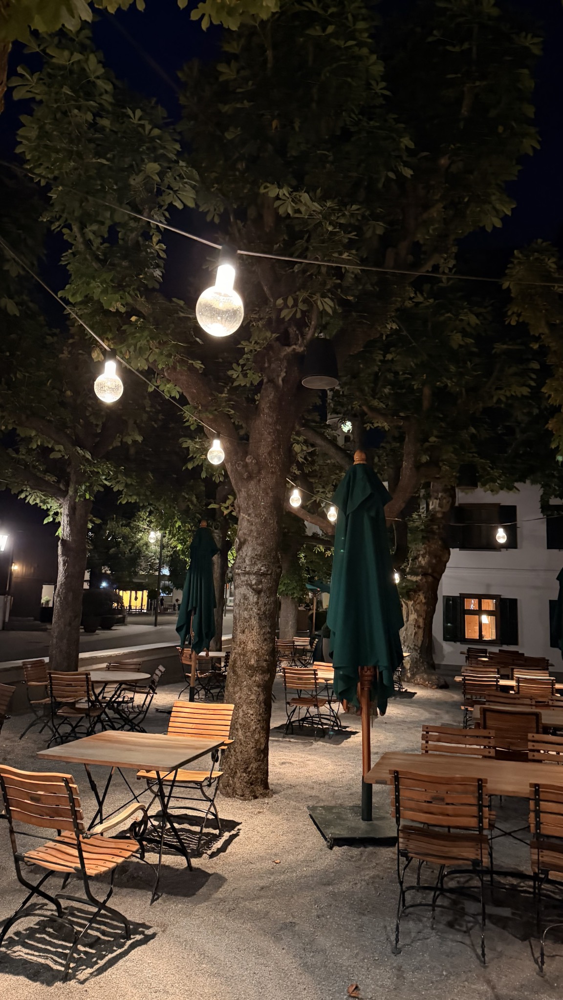 An outdoor terrace beneath leafy trees and glowing globe lights at night in Schruns, Austria