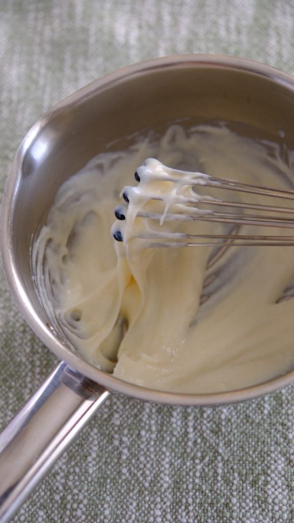 Thick cooked tangzhong clinging to a whisk in a small saucepan