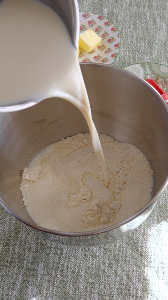 Activated milk and yeast mixture being poured into flour in a stand mixer bowl