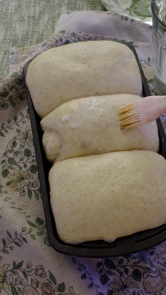 Fully proofed three-section loaf being brushed lightly with milk before baking
