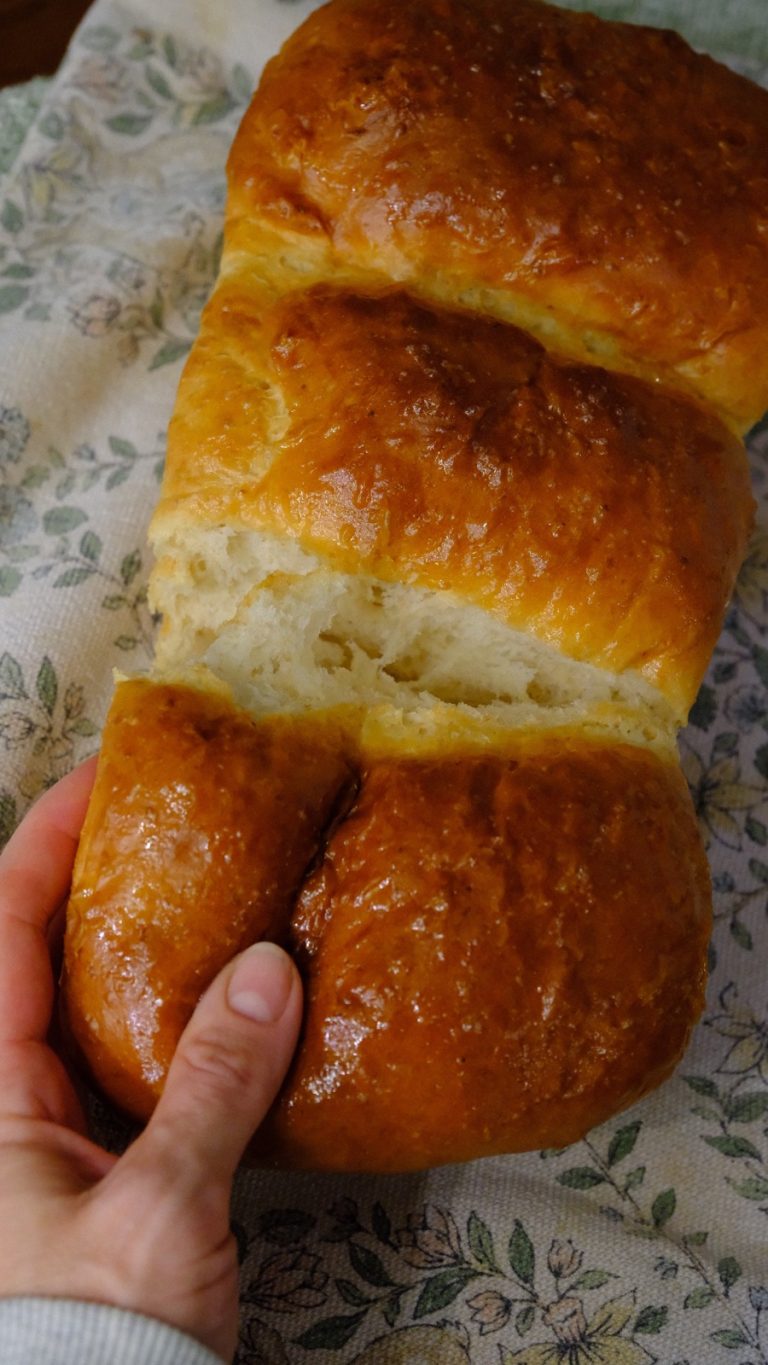 A hand pulling one soft section away from the freshly baked milk bread